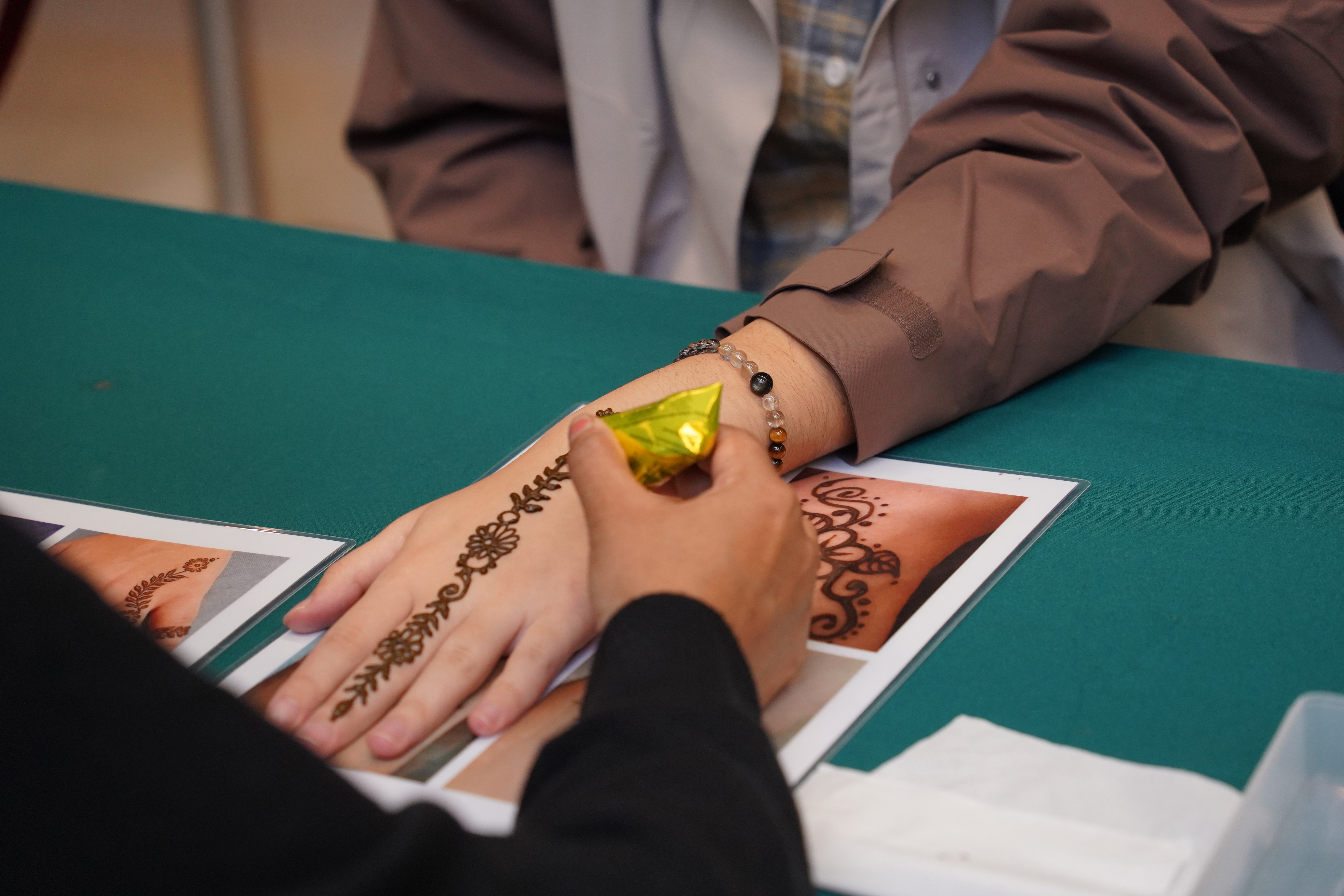 The artist is drawing henna on the students' hands.