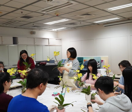 The teacher was demonstrating the procedure of making an orchid centrepiece and students were following step by step and asking their neighbouring students for help if they encountered difficulties. 導師正在示範製作蘭花擺設的步驟，學生則逐步跟上，並在遇到困難時向鄰近同學求助。