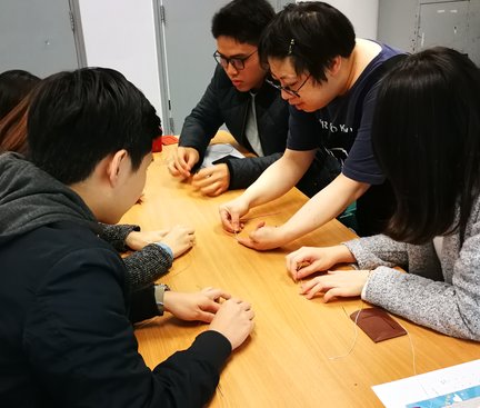 An instructor moved closer to the participants who were sitting and demonstrated how to insert the thread into the needle at the centre of the table. 導師走近參加者教授如何把針線插入卡套