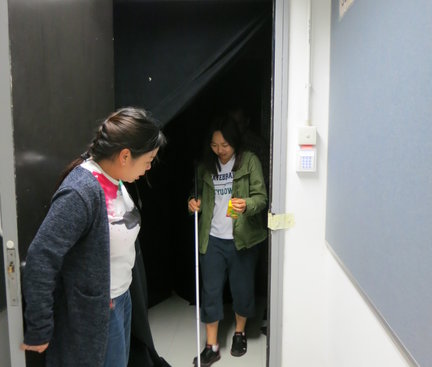One of the participants had finished her dark walking and saw the light again. From the picture, it seemed the dark scene was prepared inside a room with clothes in the dark to cover the walls and windows. 其中一位參加者完成了在黑間中行走並重見光明。從圖中可見，黑暗的場景是在房間裏由黑色的布遮蓋牆身和窗口造成。
