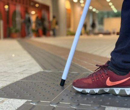 This picture was taken outside AC1 near the Wong’s International Terrace. There is a close-up to the guide tiles which were being stepped by a person in sport wear with a white cane in front. The background was blurred. 這張圖片是在楊建文學術大樓外的王氏國際廣場拍攝的。這是張特寫引路磚被穿着運動鞋的人踏着而有白手杖在鞋前的圖片。圖片背景是濛朧的。