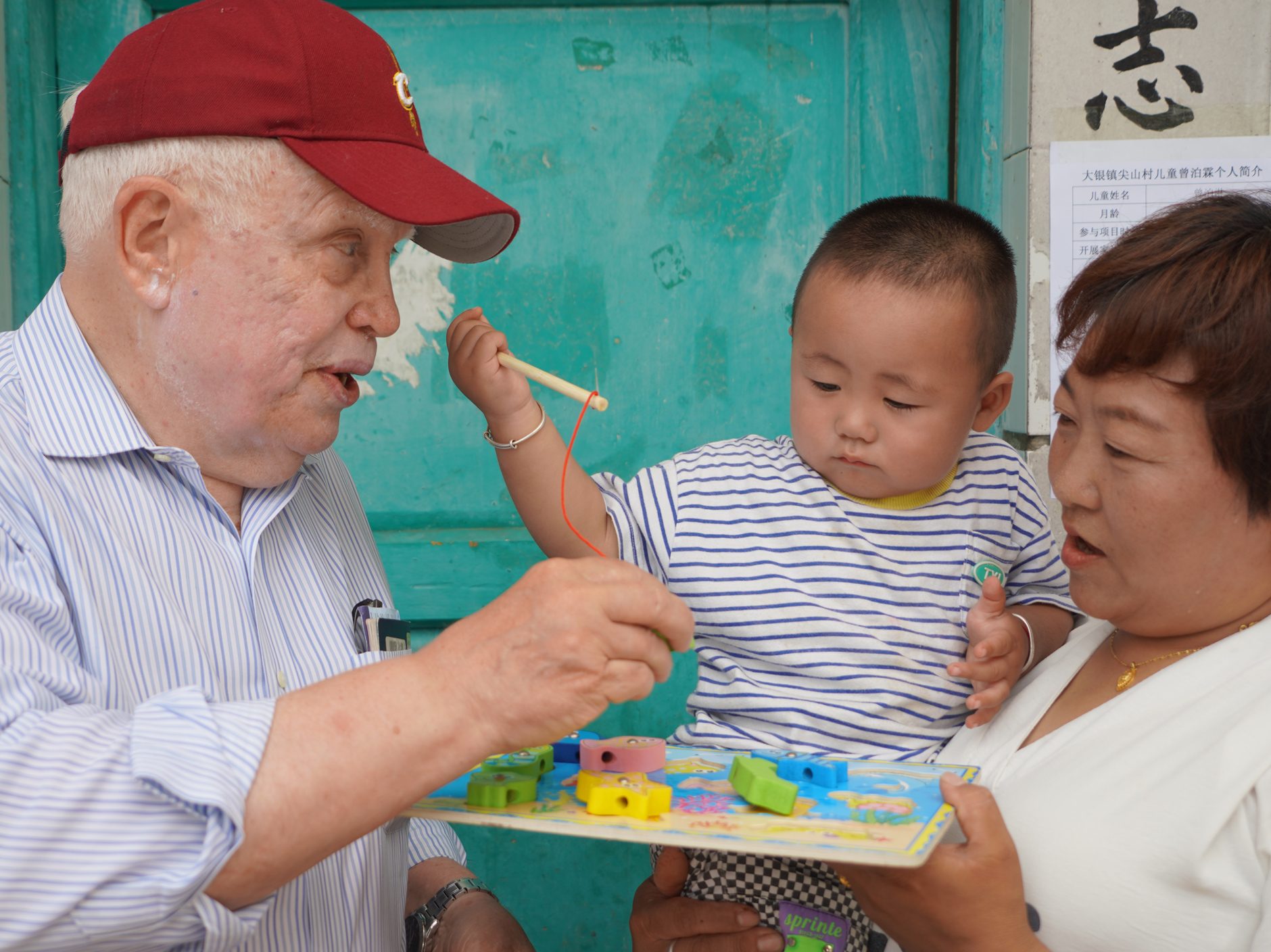 A researcher plays a toy fishing game with a young child during a China REACH home visit