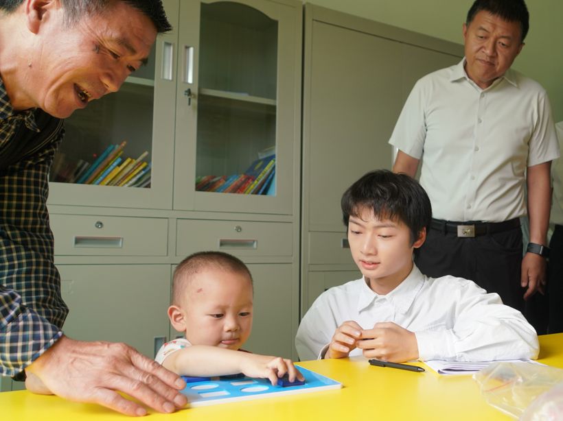 A China REACH home visitor works one-to-one with a young child on a learning activity while programme staff observe