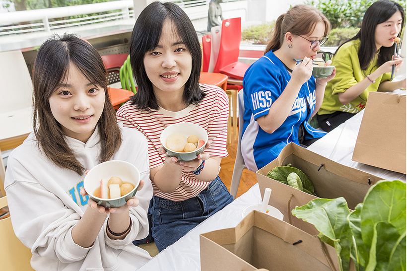 Students holding bowls of food cooked from Biodiversity Garden produce, beside bags of freshly harvested vegetables