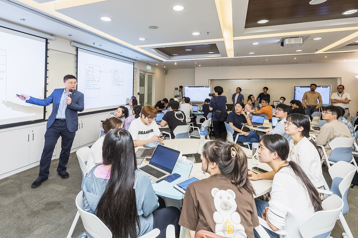 A CityUHK teacher addressing students seated at round tables with laptops in a team-based learning classroom