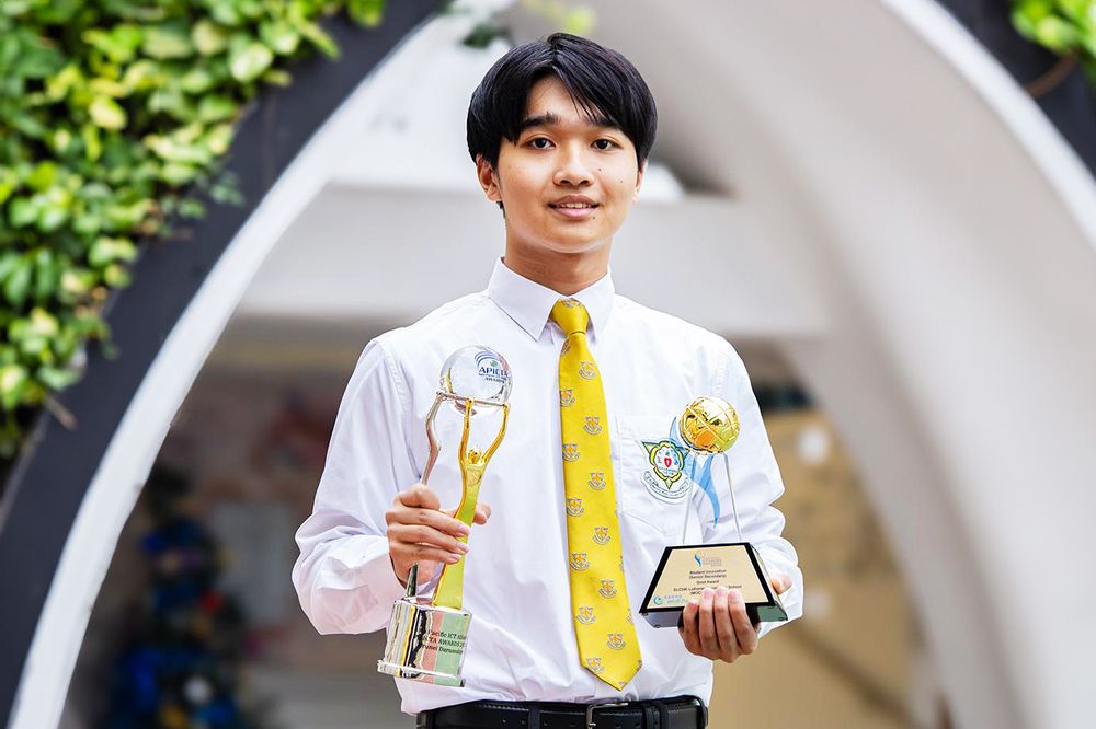 A secondary-school student in uniform holds up two APICTA award trophies