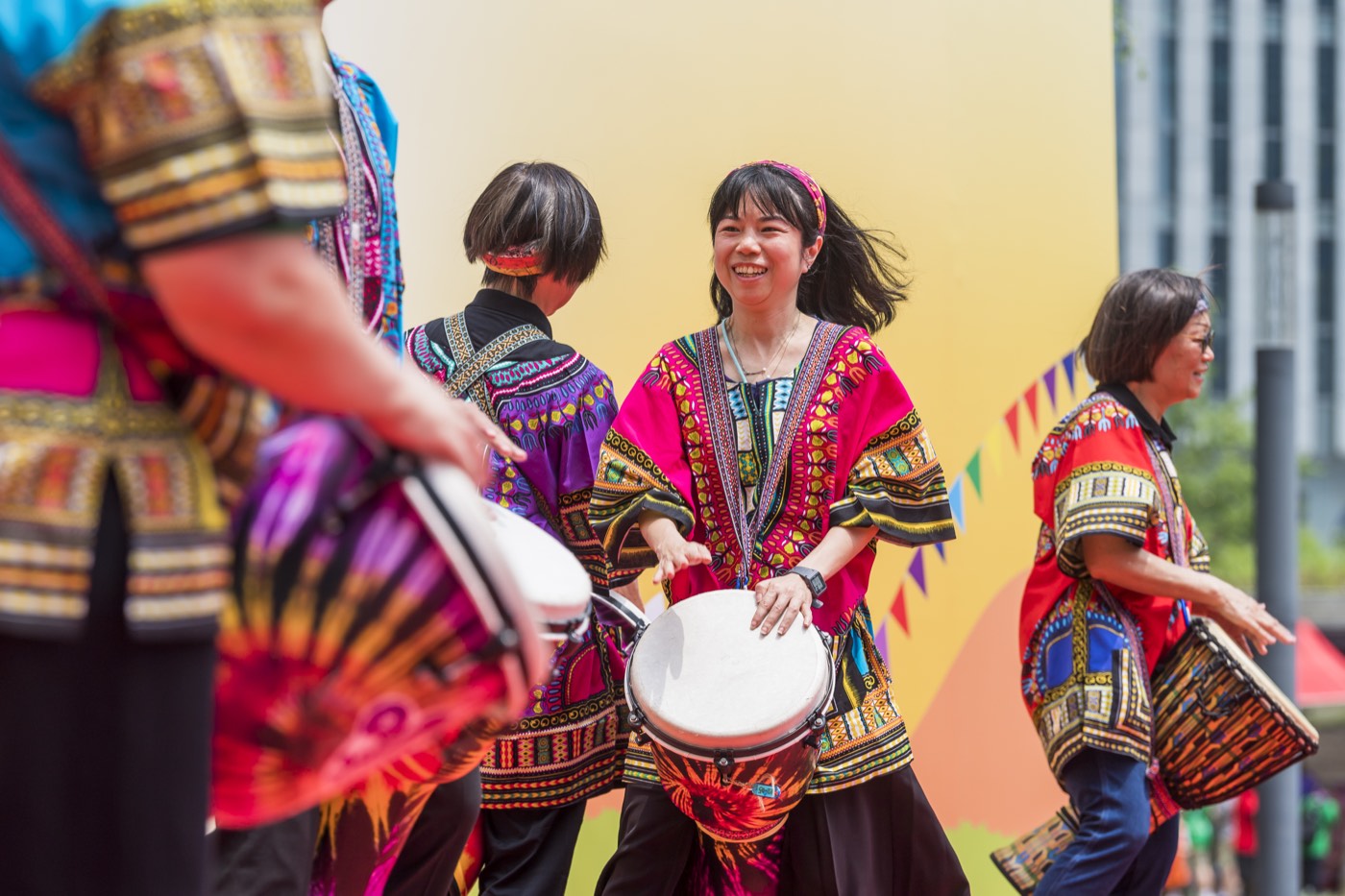 Drummers in brightly patterned costumes perform outdoors at the Together We Shine opening ceremony