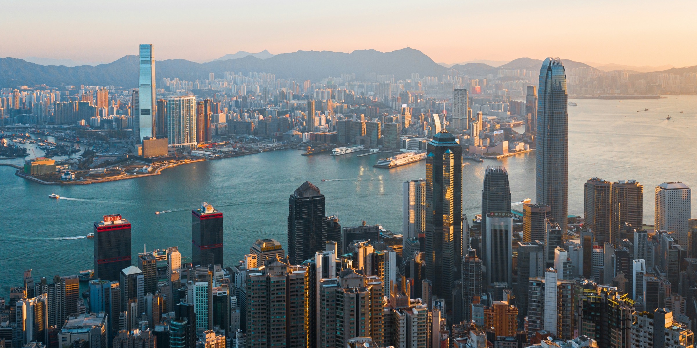 The Hong Kong skyline across Victoria Harbour at sunset, seen from above