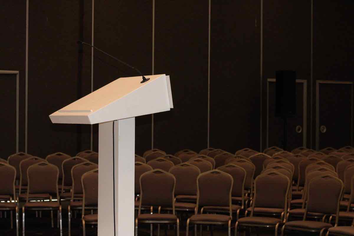 An empty lectern facing rows of chairs in a conference room