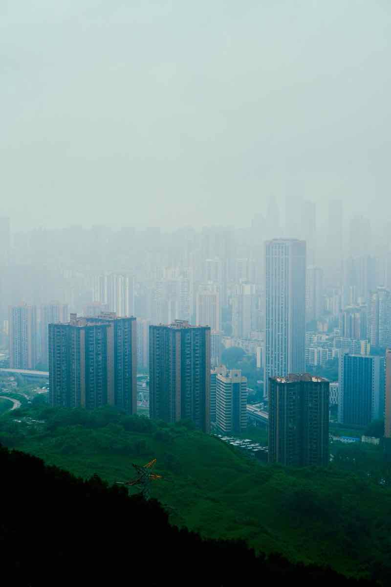 Modern high-rise towers rising through mist above a green hillside
