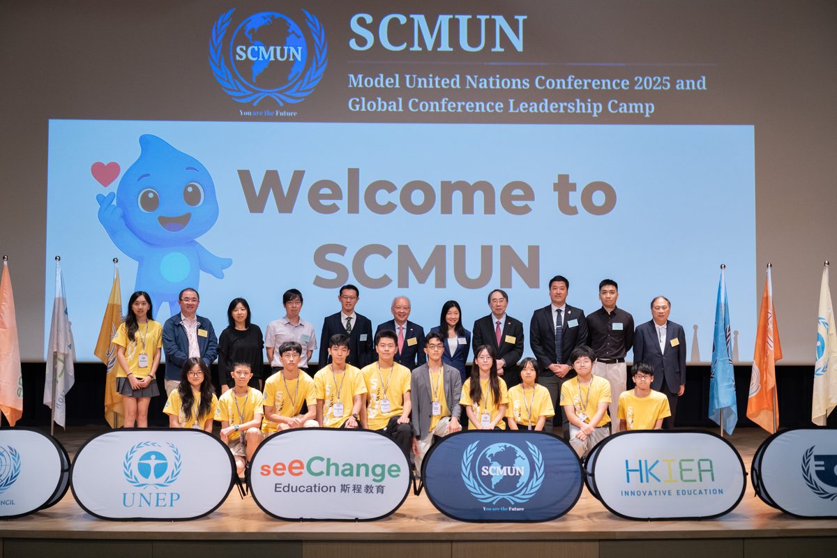 Participants and officiating guests of SCMUN 2025 on stage in front of a "Welcome to SCMUN" screen, with UNEP, See Change Education and HKIEA banners along the stage front